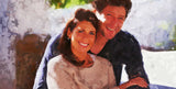 smiling couple embracing each other, with a soft-focus background of greenery and light-colored walls