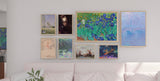 various framed art pieces, including landscapes, a portrait of a soldier in a helmet, floral paintings, and abstract art, displayed above a light pink sofa